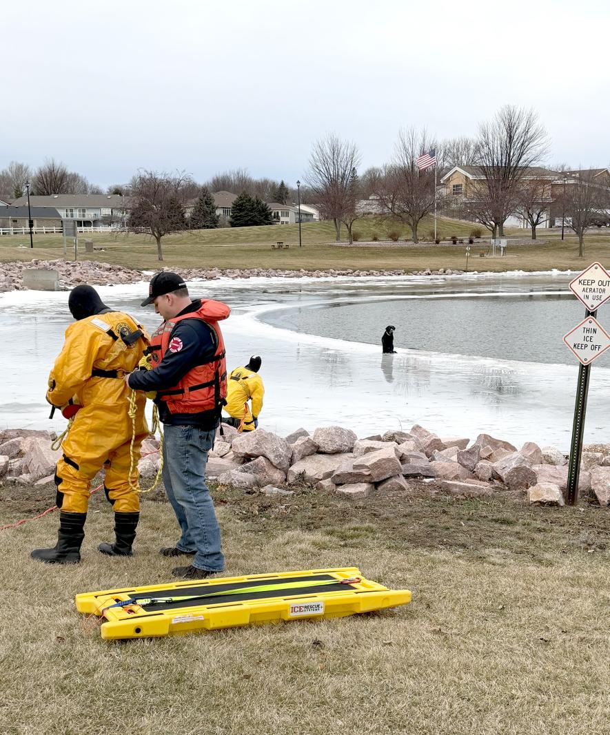 Luverne firefighter Tyler Lebrun (in red) assists Tyson Facile and Joe Juhl in suiting up to retrieve a deceased dog from the ice so that the black dog would come ashore at the Veterans Home Pond Tuesday. Shared Image