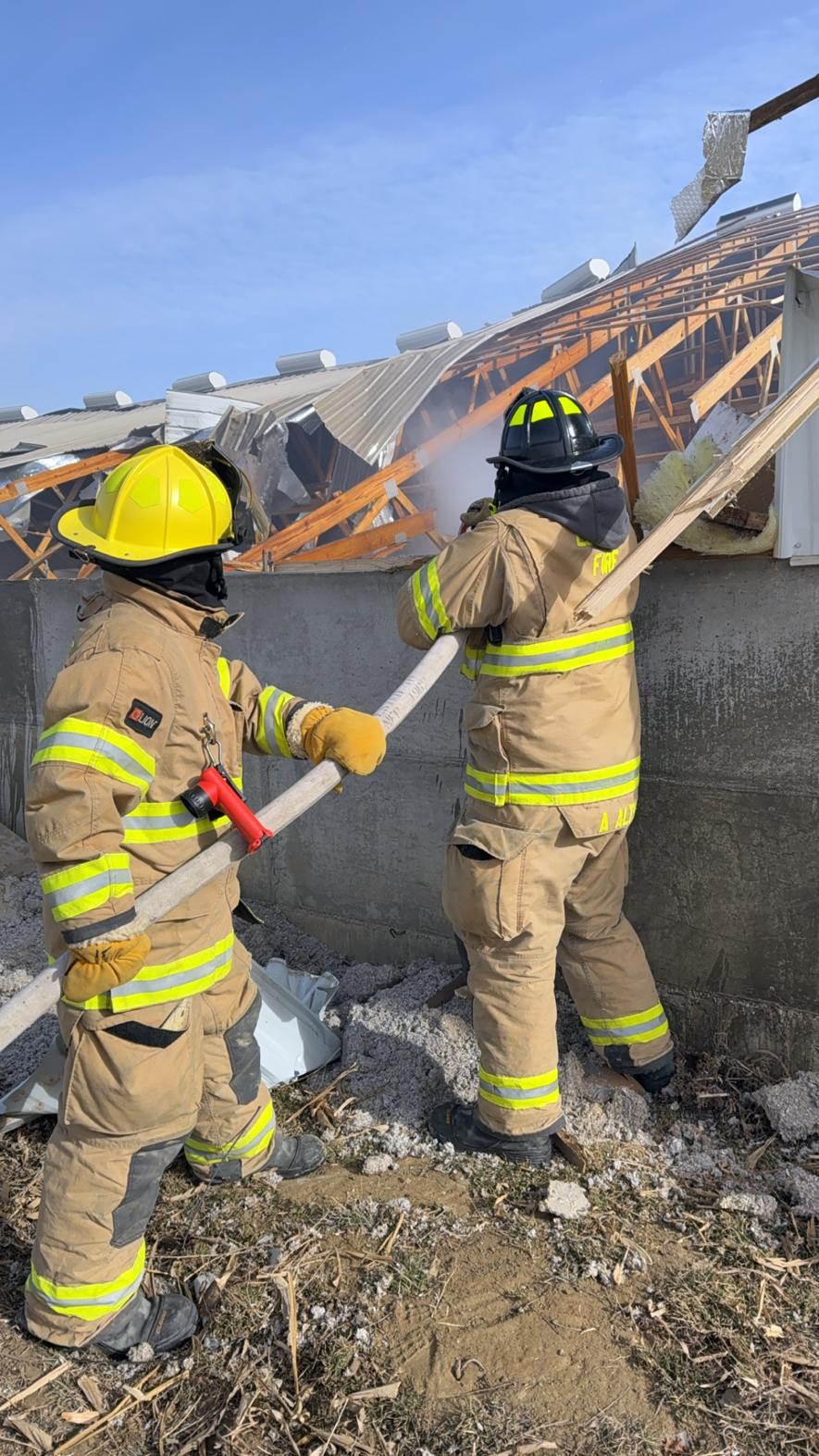 Luverne firefighters Chad Buss (left) and Aaron Altman reach over the confinement walls to extinguish flames inside the roof insulation. Photo courtesy of the Luverne Fire Department