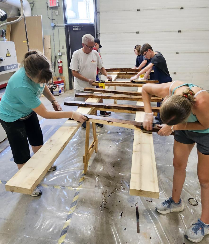 Volunteers (from left) Holly Wessels, Scott Wessels, Elijah Henrichs, Leah Mueller, Brendan Snyders and Reagan Gangestad stain wood pieces Monday afternoon that will be assembled into beds for the “Sweet Dreams” initiative. Jason Berghorst/Rock County Star Herald Photo