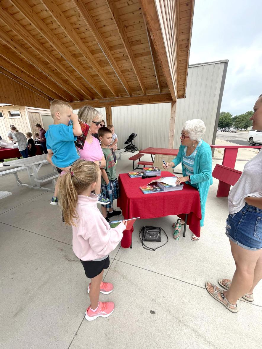She’s pictured above signing books for Ruth Aldrich, who was also getting a copy for her dad, Ed Salzer, former Luverne Elementary Principal. Aldrich is pictured at the table with Conner Aldrich (in her arms) and Hunter Aldrich. Shared Image