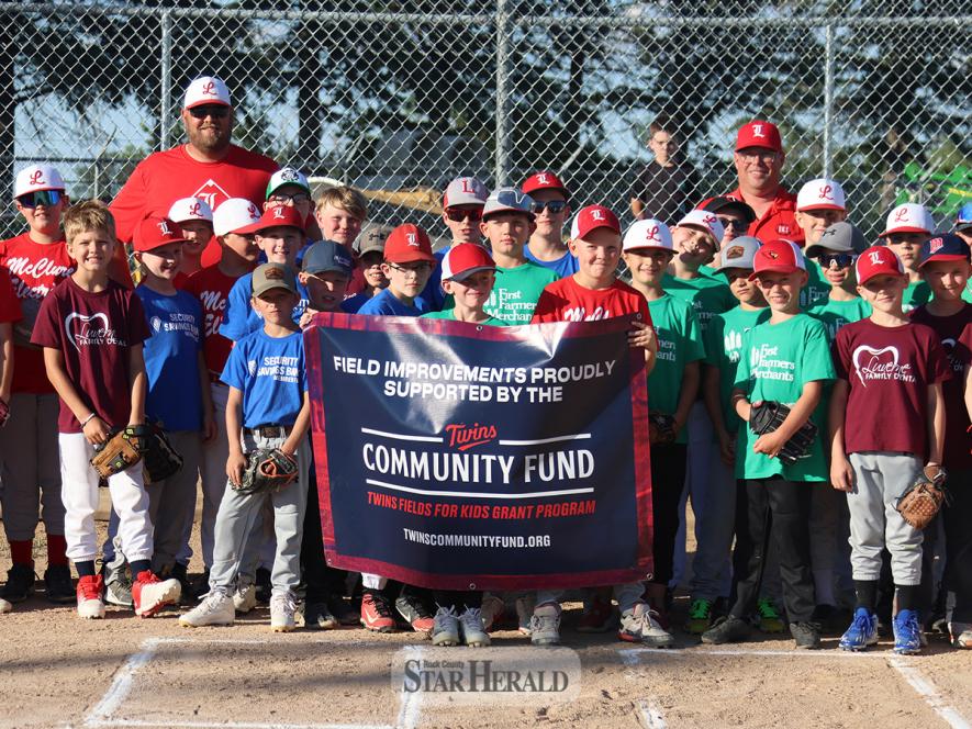 Brian Weber (back, left) and Barry Shelton (back, right) from the Luverne Baseball Association, stand with several team players presenting a banner from the Twins Fields for Kids Grant Program Tuesday, June 11, at Joe Roberts Field. 