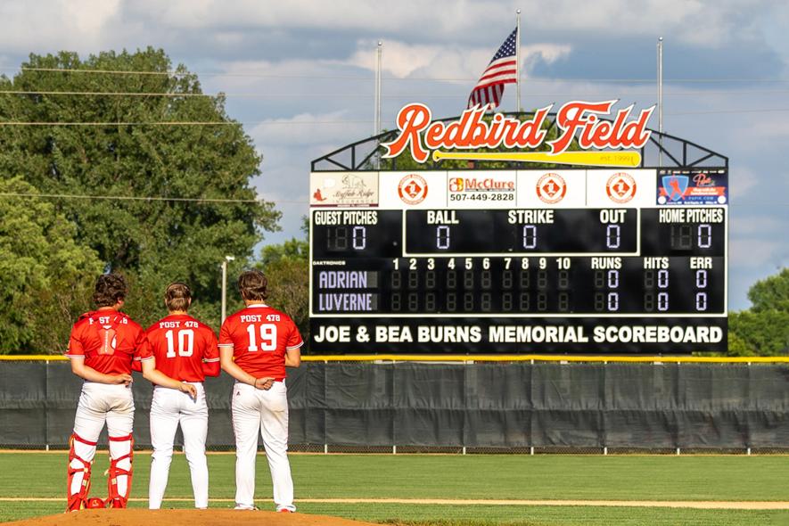 Greg Hoogeveen photo/scoreboard Luverne Senior Legion baseball team members face the new Redbird Field scoreboard June 23 during the playing of the National Anthem. Luverne beat Adrian 10-0 in the inaugural game with the new scoreboard erected in honor of Joe and Bea Burns.