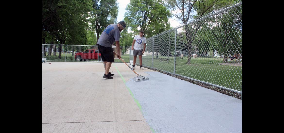 Hills Public Works supervisor Dustin Verhey (left) moves the acrylic coating onto the new pickleball courts in Jacobson Park in Hills. Assisting Verhey is Brayden Metzger.