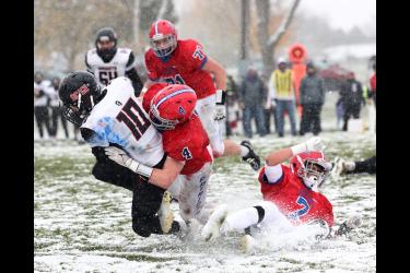 Samantha McGaffee photo: Patriot junior Beau Bakken (4) wraps up and tackles a Knights runner with sophomore Micha Bush (7) slipping on the cold, wet, snow-covered field and junior Jack Moser (71) closing in on the play. H-BC beat the Knights 28-0 at home Saturday, Oct. 28.